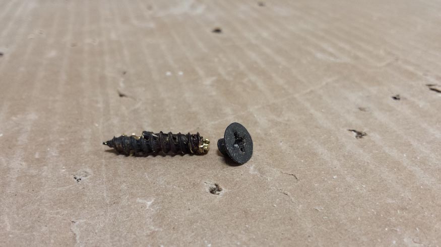 A broken screw sitting on a sheet of cardboard.